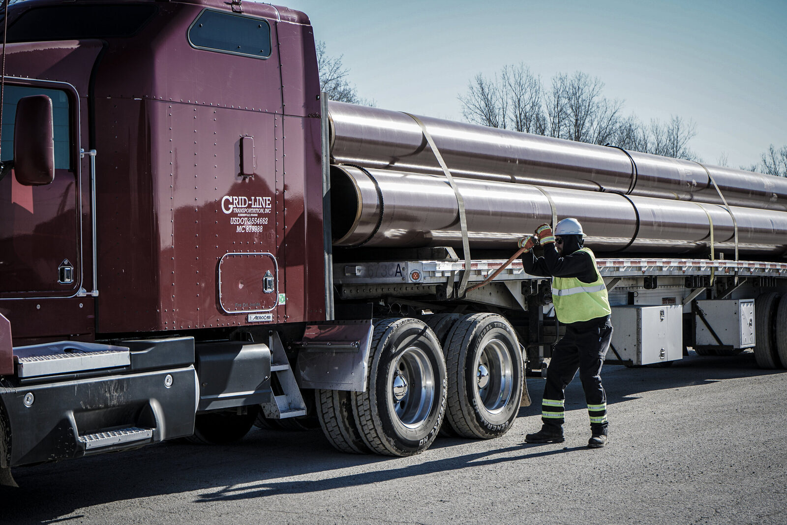 Grid-Line driver chaining stainless steel pipes onto a flatbed